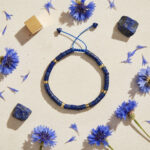 Bracelet lapis-lazuli heishi doré en flat lay avec pierres brutes et fleurs bleues