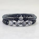 Gros plan d'un ensemble de deux bracelets homme en hématite, onyx noir et jaspe paysage gris sur fond pierre claire