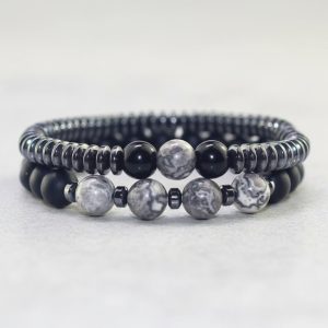 Gros plan d'un ensemble de deux bracelets homme en hématite, onyx noir et jaspe paysage gris sur fond pierre claire