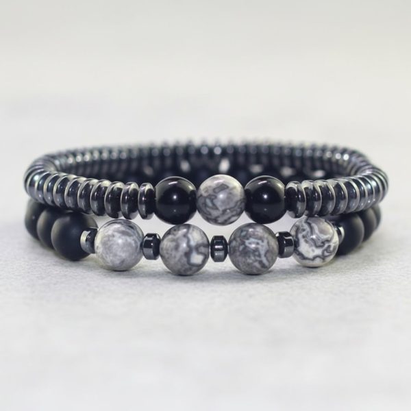 Gros plan d'un ensemble de deux bracelets homme en hématite, onyx noir et jaspe paysage gris sur fond pierre claire