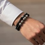 Poignet d'un homme portant un ensemble de deux bracelets élastiques en hématite, onyx noir et jaspe paysage gris