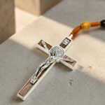 Collier chapelet bois homme pendentif crucifix argenté marron gros plan détail INRI sur béton