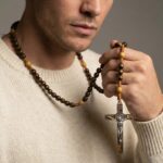 Collier chapelet bois homme pendentif crucifix argenté marron porté sur pull crème