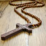 Collier chapelet homme pendentif crucifix en bois naturel sculpté marron avec perles de bois posé sur surface en bois