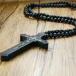 Collier chapelet homme pendentif crucifix en bois sculpté noir et perles de bois posé sur surface en bois
