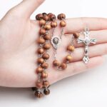 Collier chapelet homme perles bois naturel marron pendentif crucifix argenté tenu dans une main