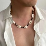 Collier homme coquillages cauri naturels et perles noires porte chemise blanche ouverte