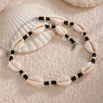Collier homme coquillages cauri naturels et perles noires pose sur sable avec coquillages