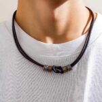 Collier homme cordon cuir marron nœud central anneaux métal bronze porté sur t-shirt blanc vue cou lifestyle
