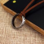 ollier homme cordon cuir daim marron pendentif anneau acier argenté vieilli avec inscriptions gravées posé sur fond lin