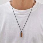 Collier homme cordon noir pendentif barre pierre naturelle oeil de tigre ambre porté sur t-shirt blanc vue cou