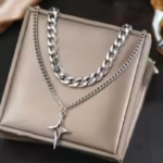 Collier homme double couche chaîne argentée pendentif étoile posé sur pochette beige