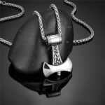 Collier homme pendentif hache viking acier inoxydable argent pose contre pierre noire vue angle