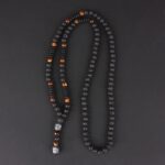Collier homme pierre œil-de-tigre noir marron 70 cm disposé en U sur fond gris foncé pendentif bouddha argenté