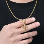 Homme tenant un collier pendentif croix gothique en acier inoxydable doré gravure arabesque, t-shirt noir