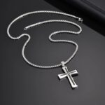 Collier pendentif croix homme acier inoxydable argent noir posé sur surface noire