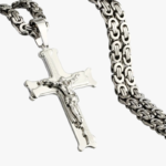 Gros plan pendentif crucifix en acier inoxydable argenté avec chaîne maille byzantine fond blanc