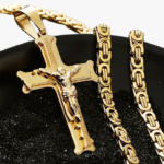 Collier pendentif crucifix en acier inoxydable doré et chaîne maille byzantine posés sur plateau noir