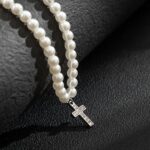 Collier perle homme blanc pendentif croix strass argentée posé sur surface noire texturée gros plan croix