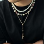 Collier perle homme multirangs blanc pendentif croix dore cristaux colores porte sur pull noir