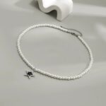 Collier homme perle blanche nacrée pendentif étoile argentée zircon noir posé sur fond gris
