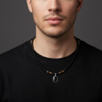 Collier ras-de-cou perlé noir homme onyx œil de tigre pendentif pierre argentée porté sur t-shirt noir fond gris