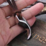 Collier viking homme griffe loup pendentif argente poli tenu en main sur fond bois